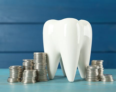 A ceramic model of a tooth and coins on a light blue wooden table