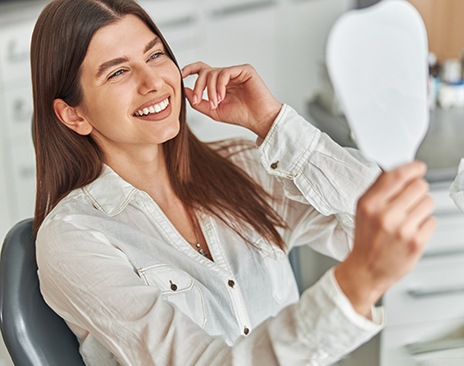 A happy woman admiring her smile by using a hand mirror